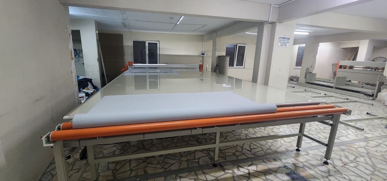 میز برش پارچه صنعتی CNC با رول پارچه بارگذاریشده روی میز گسترش